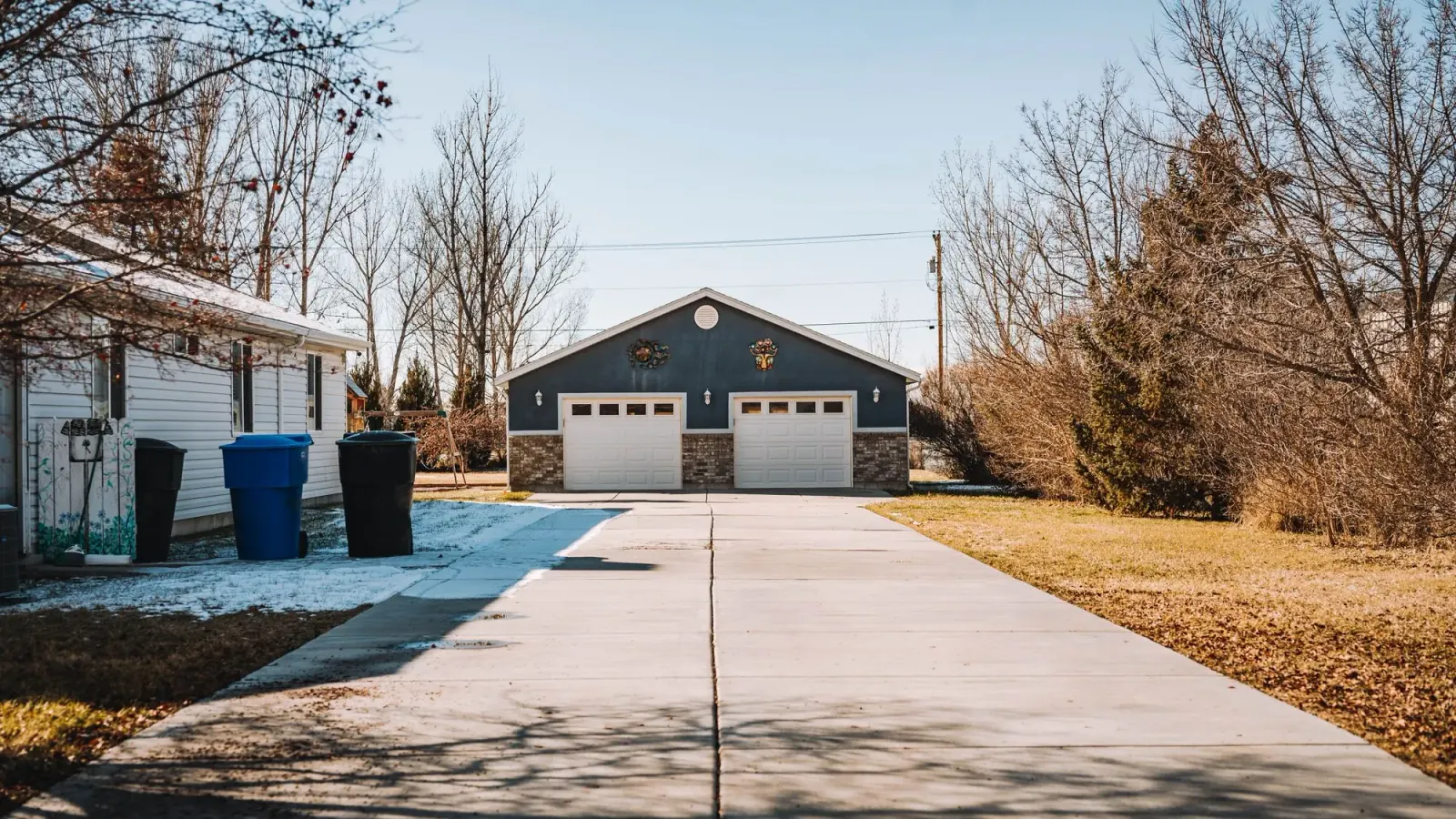 Detached garage with a long concrete driveway on a bright winter afternoon