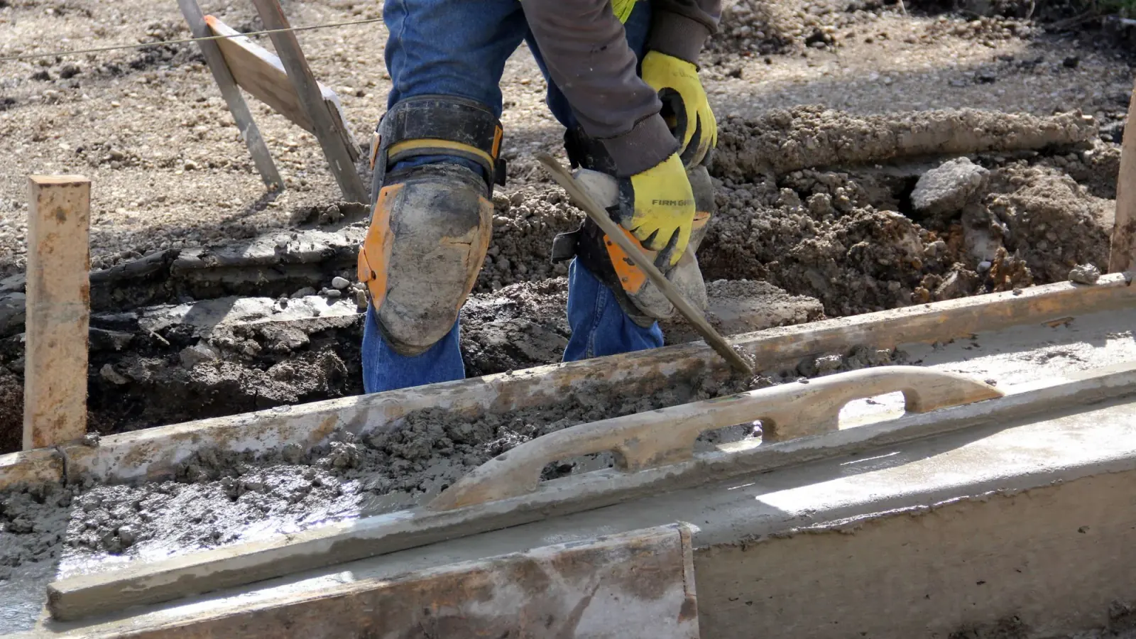 Worker running a bull float across freshly poured concrete inside its forms