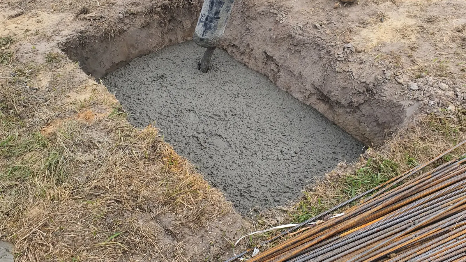 Concrete poured into a footing trench with reinforcement bars stacked alongside