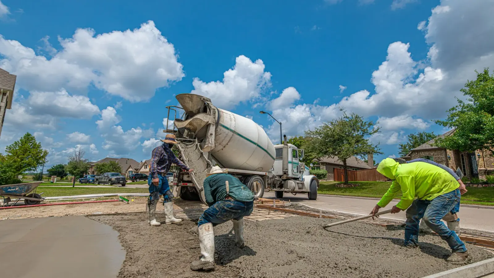 Crew placing and screeding concrete for a residential driveway beside a mixer truck