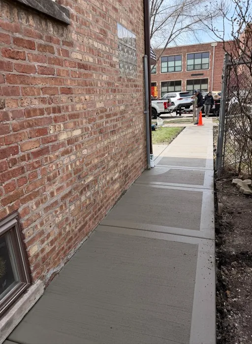 New broom-finished concrete walkway alongside a brick building