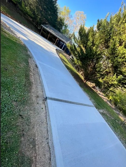 New curved concrete driveway with integrated channel drain on a wooded lot